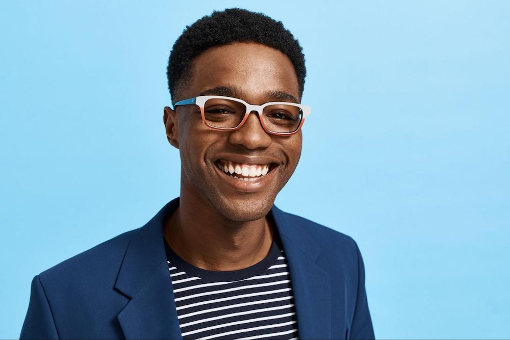 A man smiling while wearing glasses and a blue blazer.